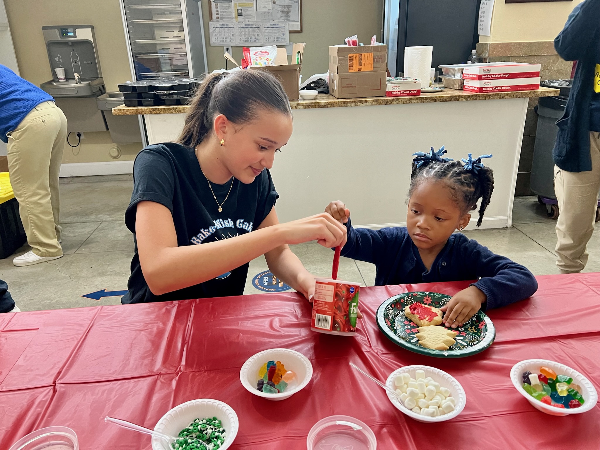 Bake-A-Wish volunteer helping child with cookie decorating at holiday party