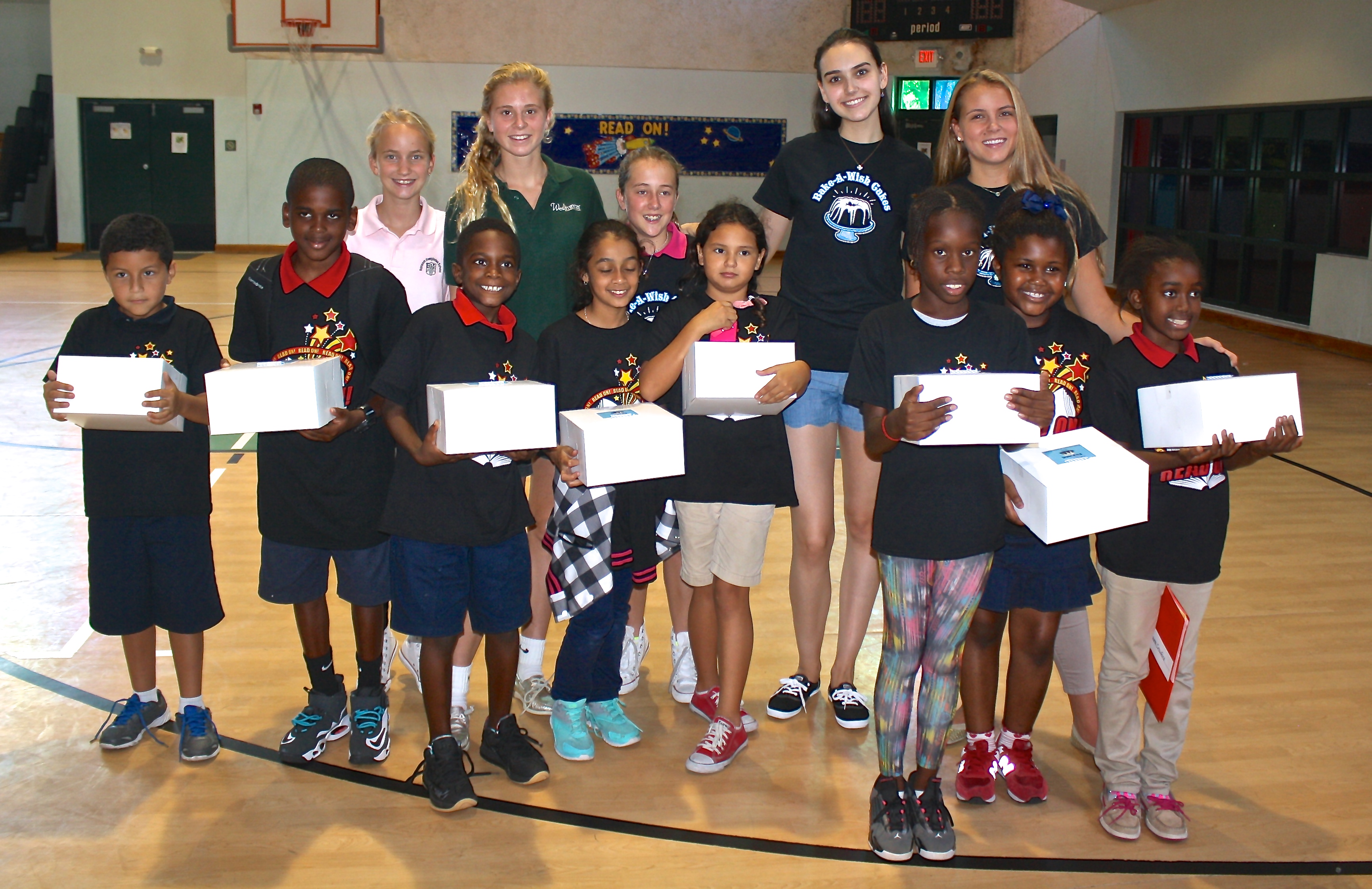 Group photo of children and volunteers with cake boxes in school gymnasium